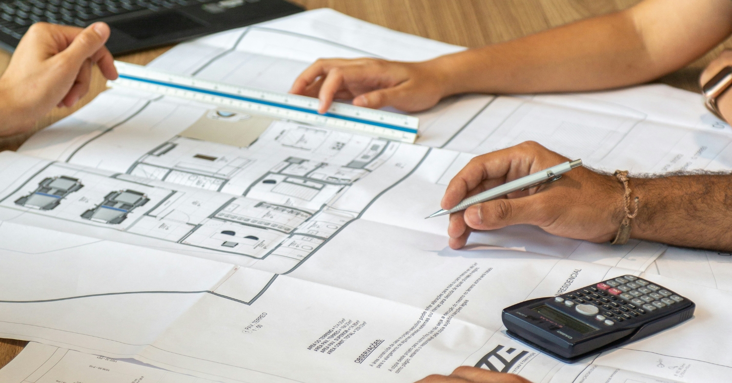 Architectural plans being reviewed with a scale, pencil, and calculator for an ADU project