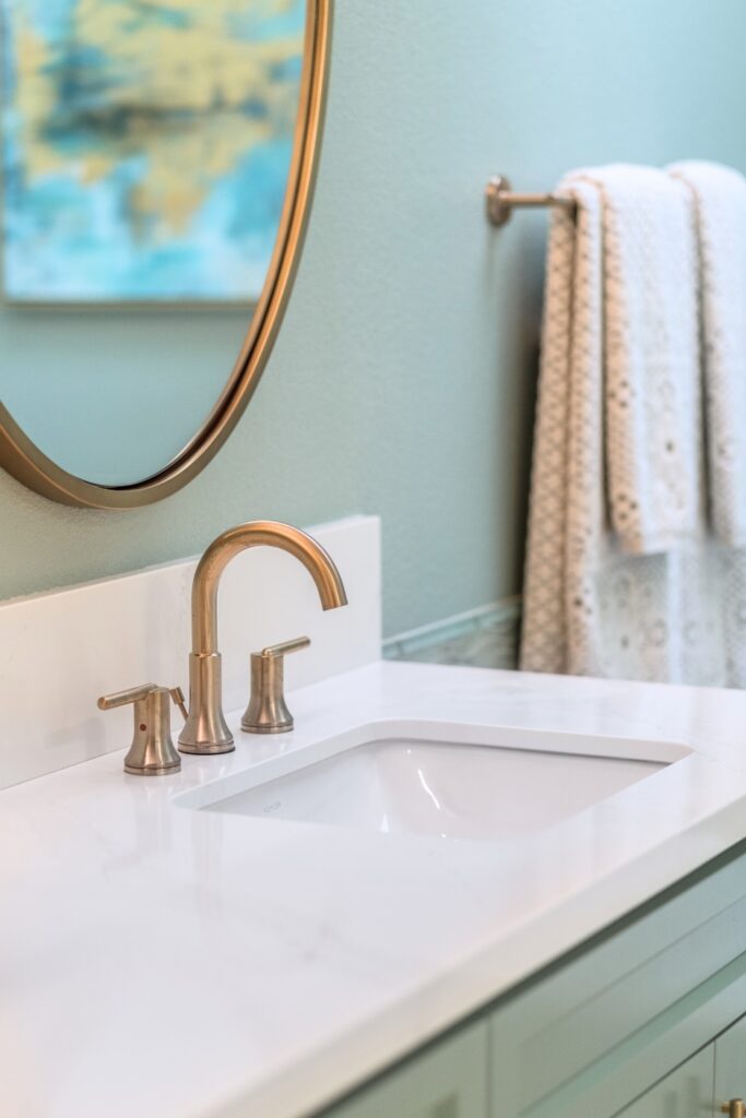 Primary bathroom vanity with brass faucet, round brass mirror and quartz countertop