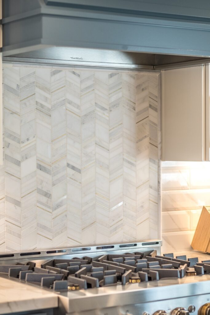Chevron marble mosaic backsplash tile with brass inlay accents behind kitchen range