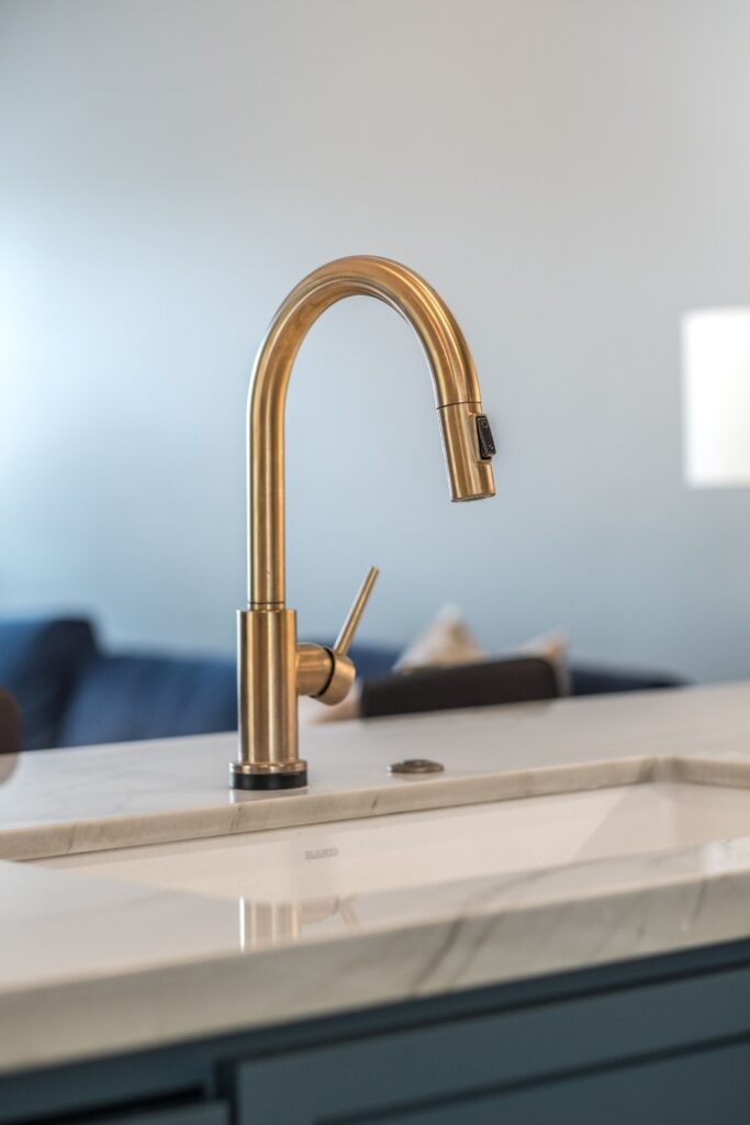 Brass gooseneck faucet at kitchen island sink with quartz countertop and blue cabinetry