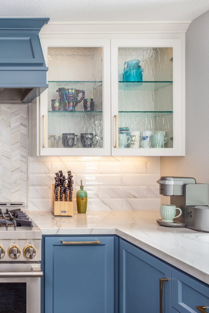Glass-front cabinets displaying glassware above marble subway tile backsplash and blue cabinetry