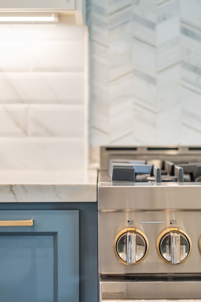 Range knobs with brass trim against white subway tile and chevron mosaic backsplash