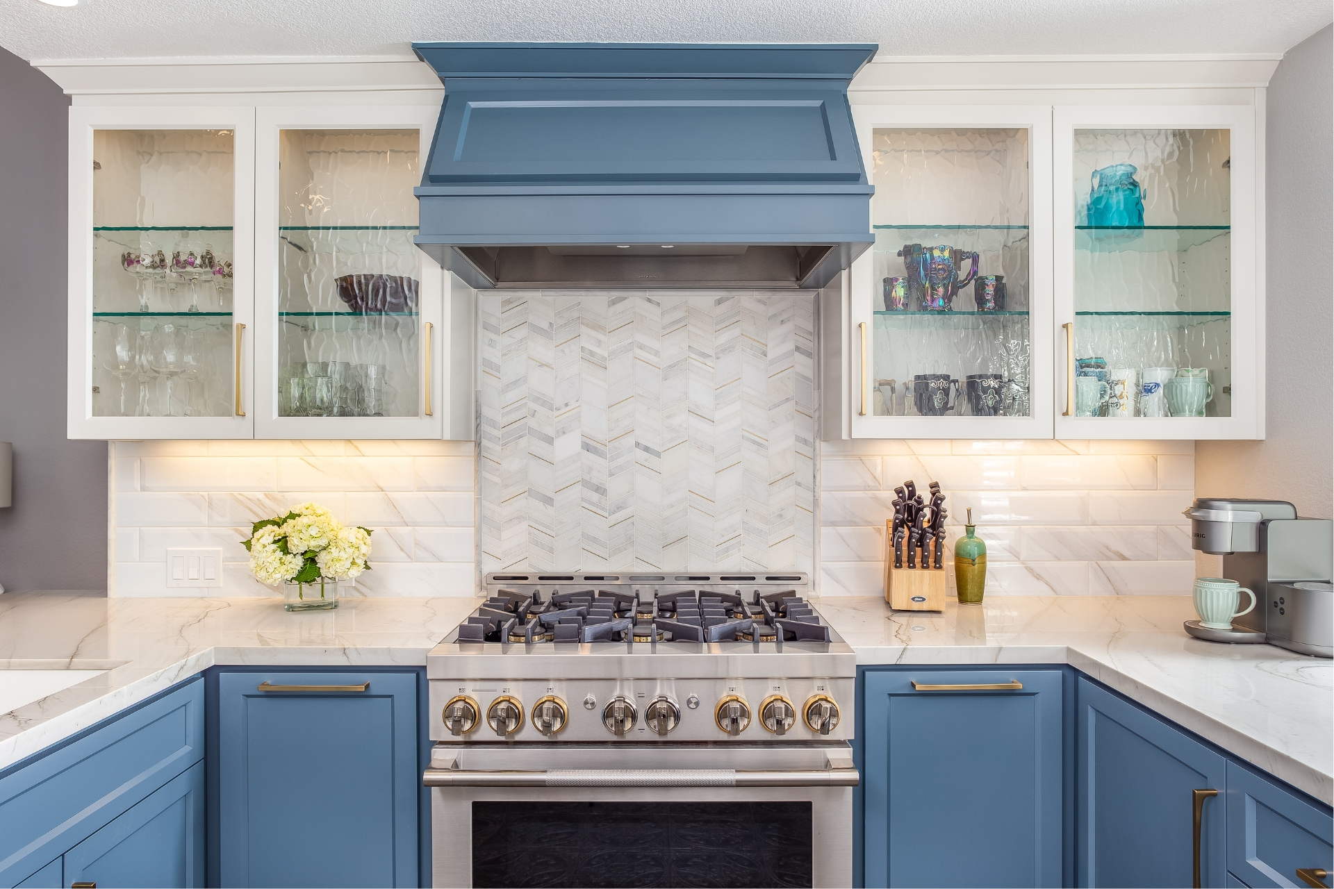Kitchen remodel with blue range hood, chevron marble mosaic backsplash, glass-front cabinets and gas range
