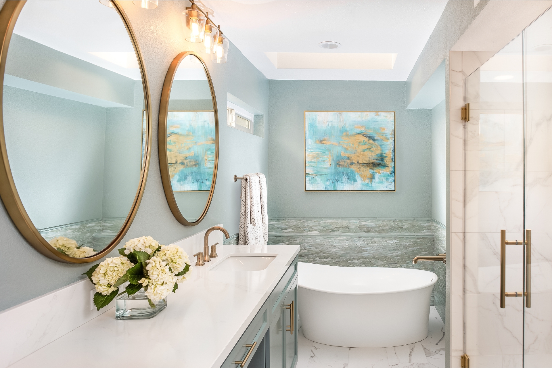 Primary bathroom with freestanding soaking tub, sea-glass mosaic tile, round brass mirrors and quartz vanity
