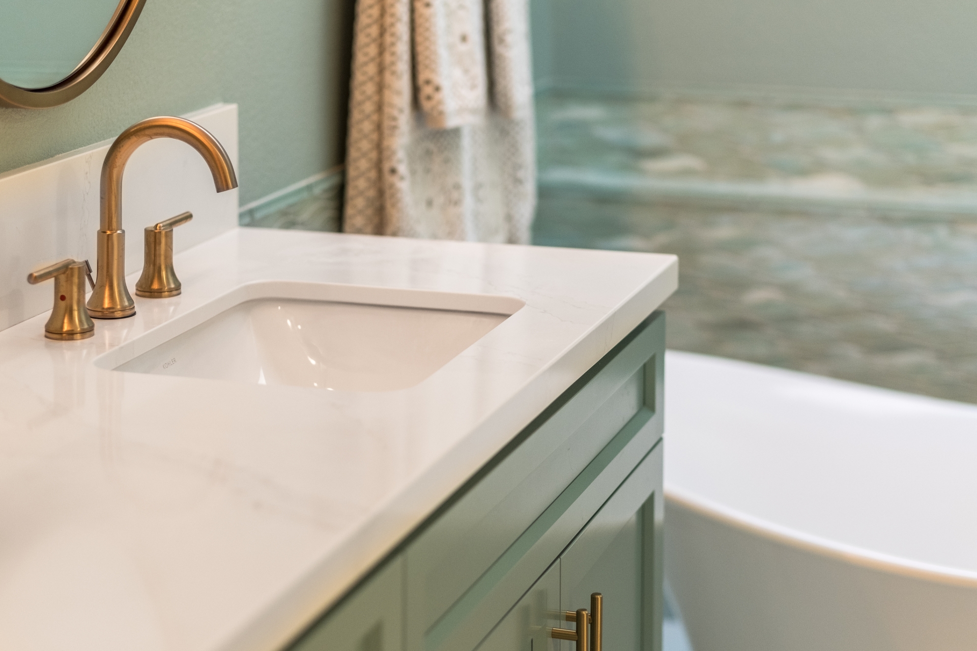 Bathroom vanity detail with brass faucet, quartz counter and undermount sink near freestanding tub