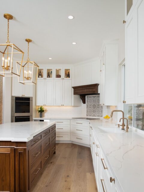 Carlsbad kitchen remodel with dark wood island, white cabinetry, veined counters, brass pendants and patterned cooktop surround.