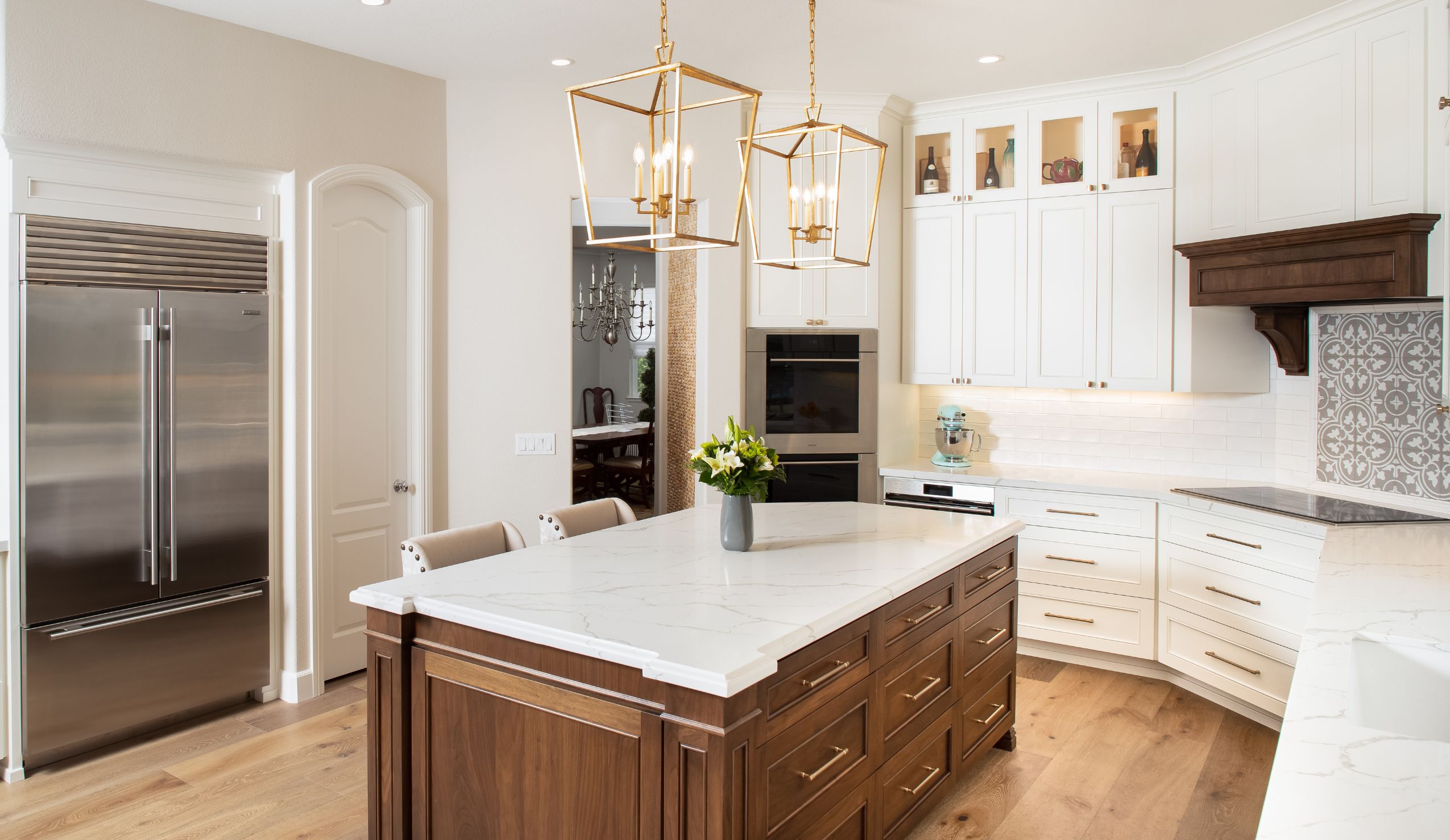 Wide view of Carlsbad kitchen remodel with wood island, white cabinetry, stainless appliances and brass lantern pendants.