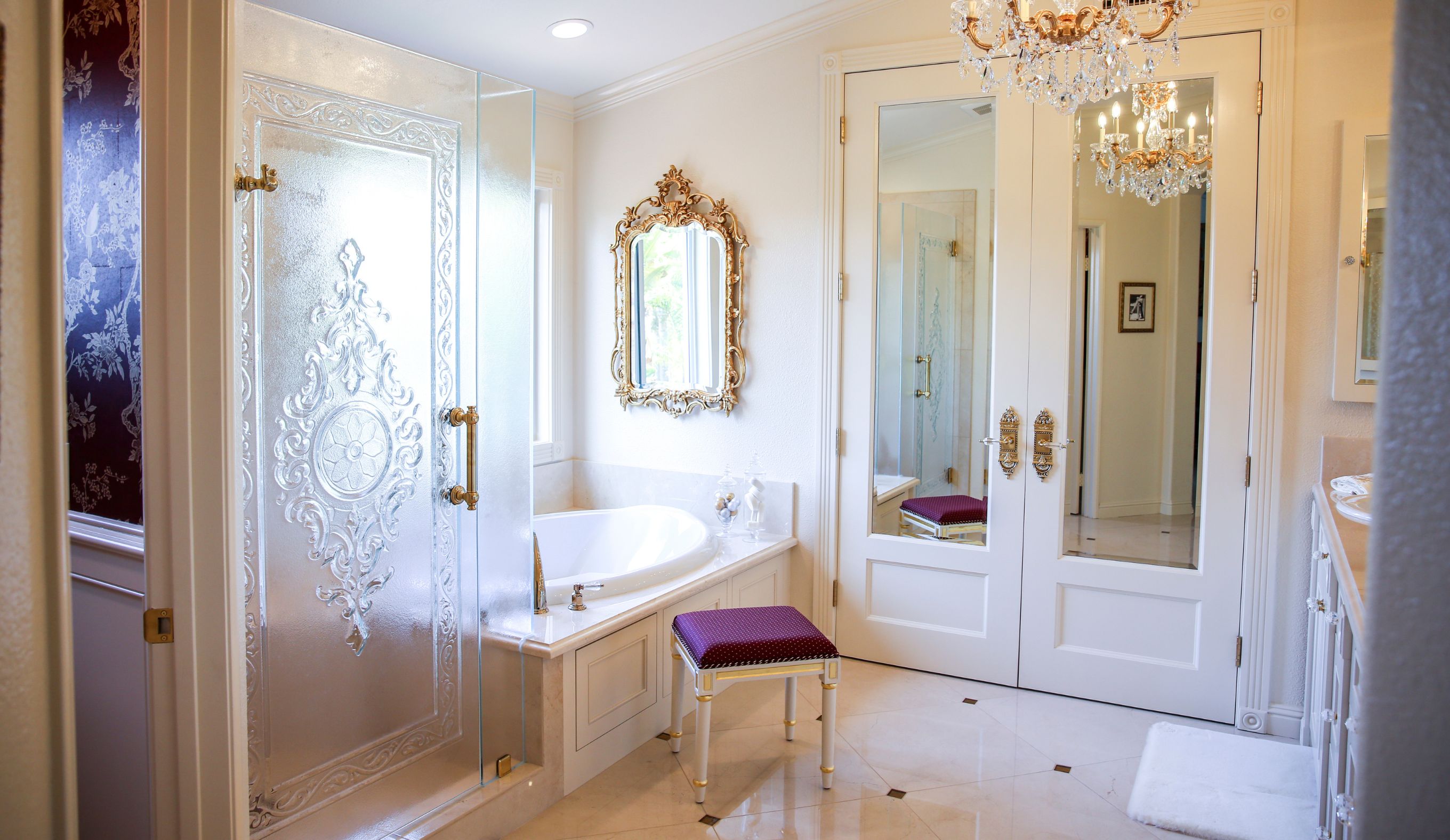 Carlsbad primary bathroom with etched glass shower, soaking tub, crystal chandelier, mirrored double doors and gold hardware.