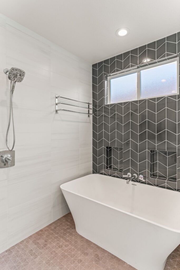 Freestanding tub with wall-mounted faucet, twin niches, frosted window and charcoal chevron tile.