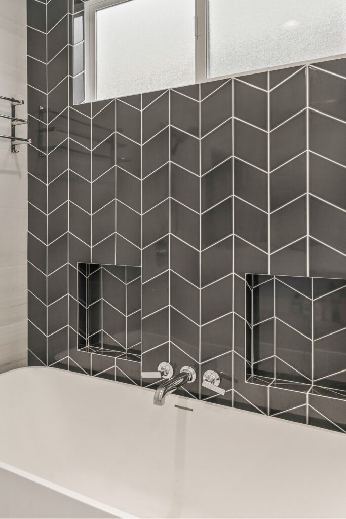 Tub surround with charcoal chevron tile, two recessed niches, wall-mounted filler and frosted window.