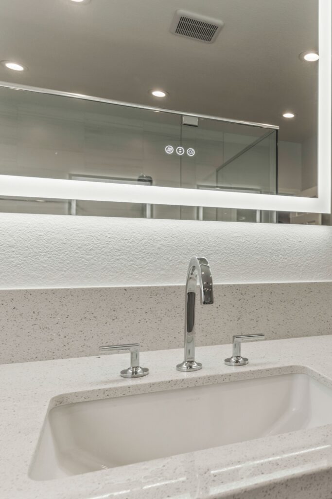 Undermount bathroom sink with chrome widespread faucet, speckled counter and backlit mirror.
