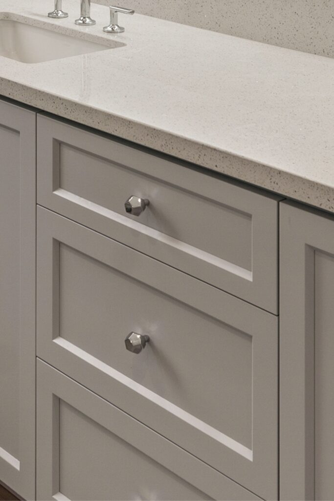 Close-up of gray vanity drawers with recessed panels, faceted chrome knobs and white speckled counter.