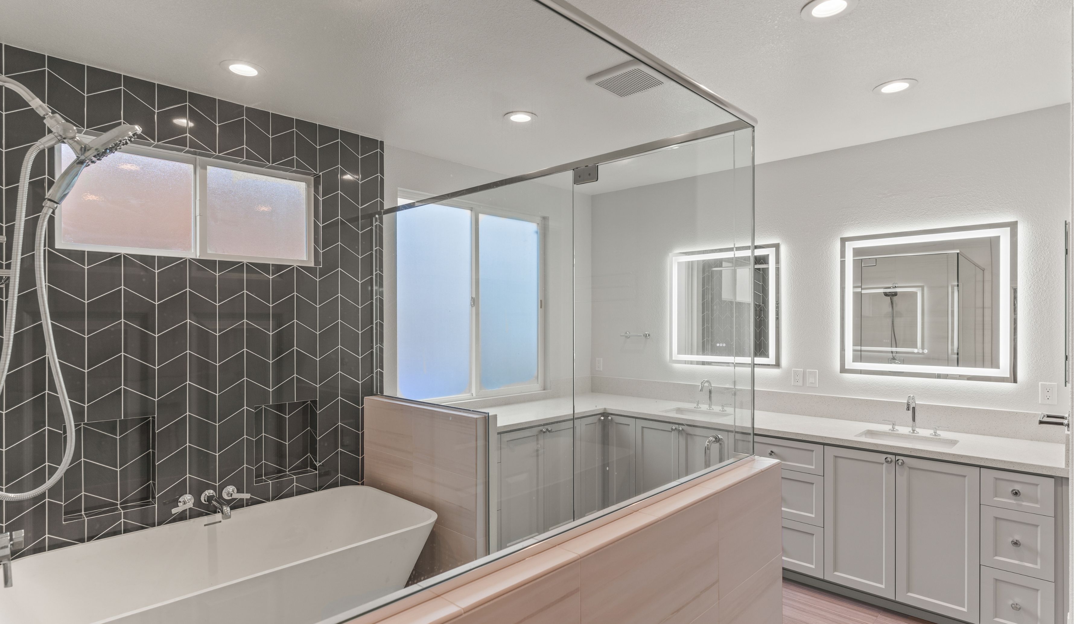 Wide Carmel Valley bathroom remodel with double vanity, illuminated mirrors, glass shower and freestanding tub.