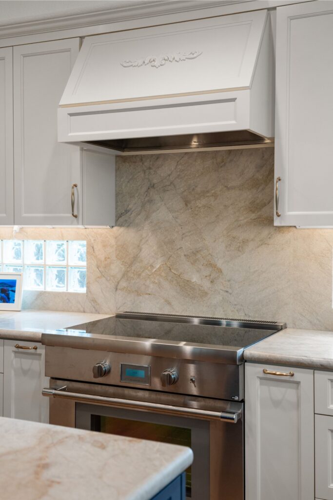 Kitchen cooking wall with paneled vent hood, stainless range and full-height veined stone backsplash.