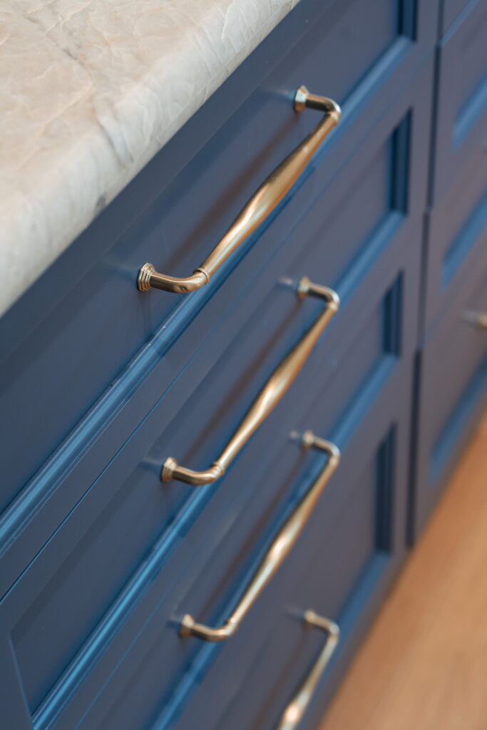 Blue kitchen island drawers with brass pulls and a light veined stone countertop.