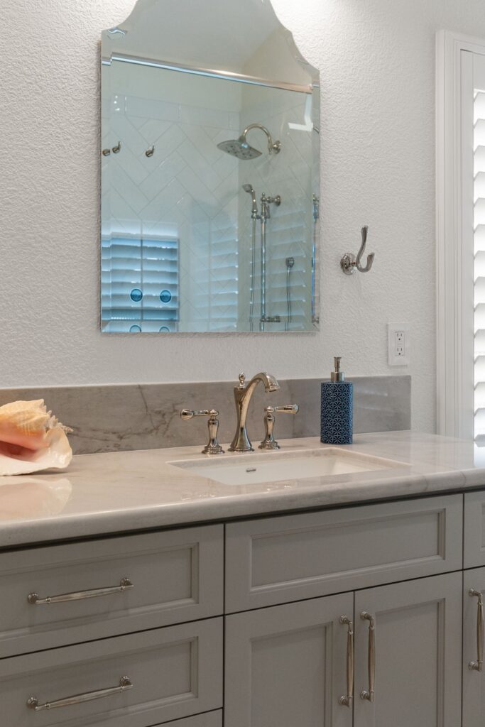 Bathroom vanity with gray cabinetry, stone counter, undermount sink, decorative mirror and polished metal fixtures.
