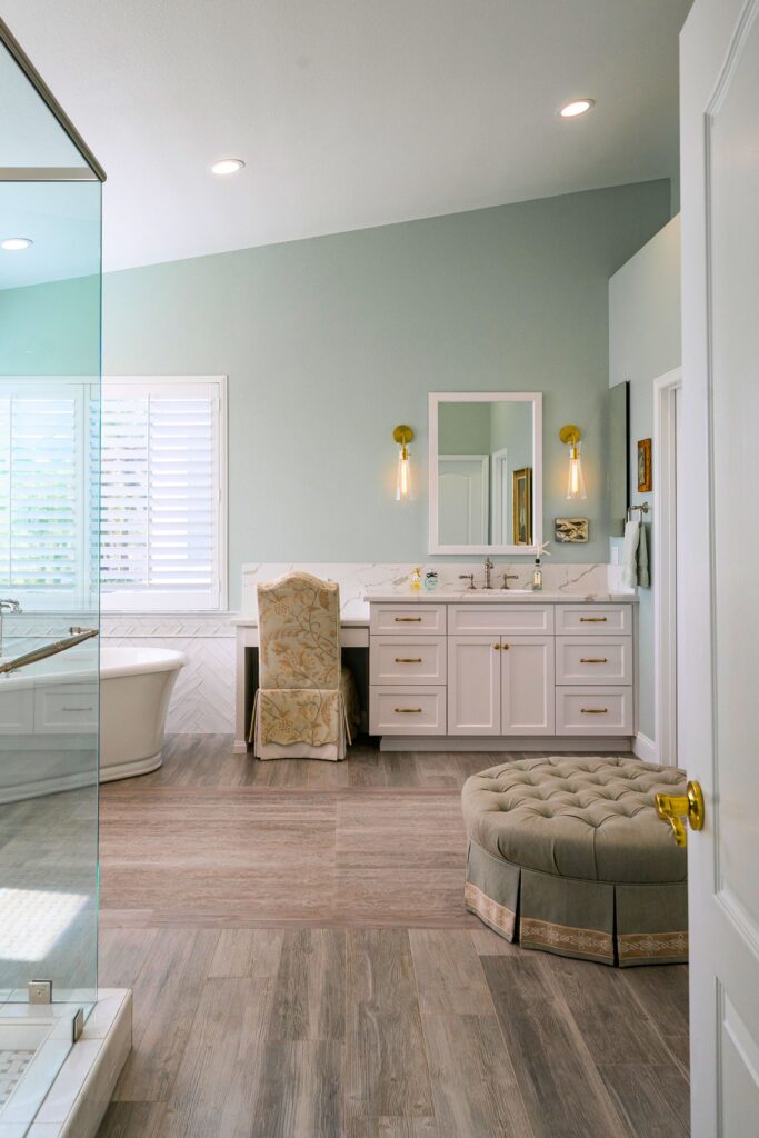 Primary bath with white vanity, veined countertop, brass sconces, freestanding tub and glass shower enclosure.