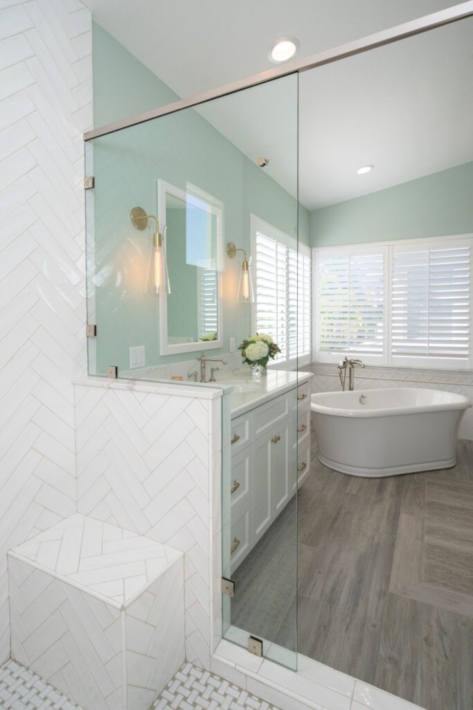 Primary bath with glass-enclosed shower, built-in bench, white herringbone tile, vanity and freestanding tub.