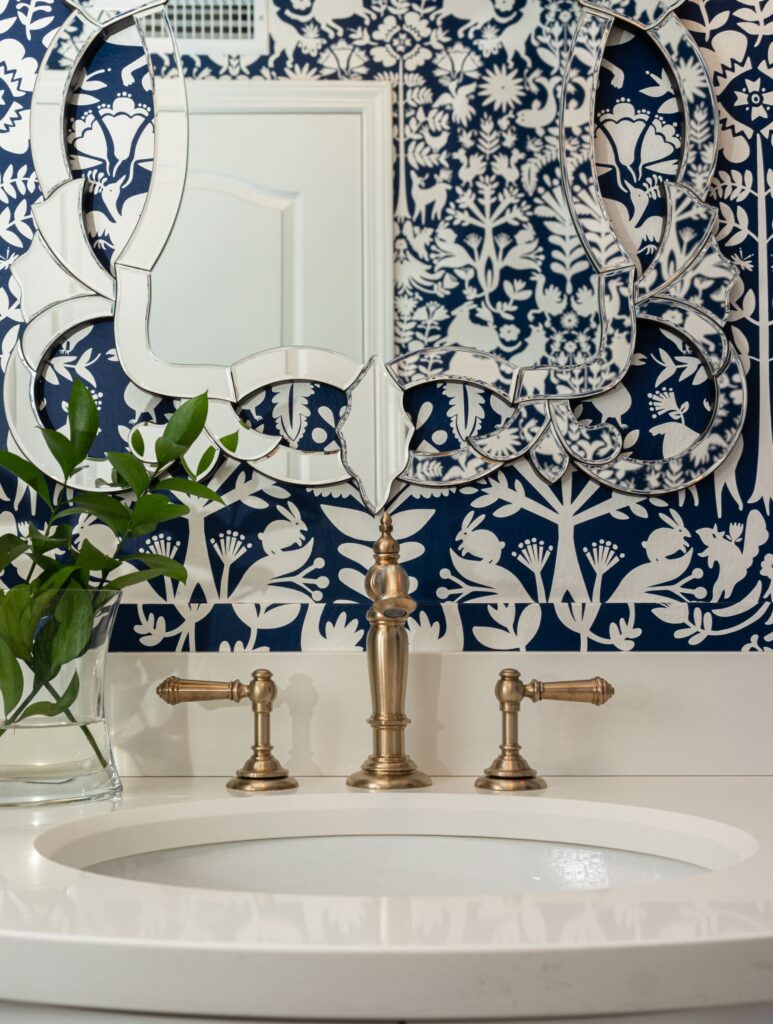 Carmel Valley powder room remodel with navy floral wallpaper, brass faucet, white sink and decorative mirror.
