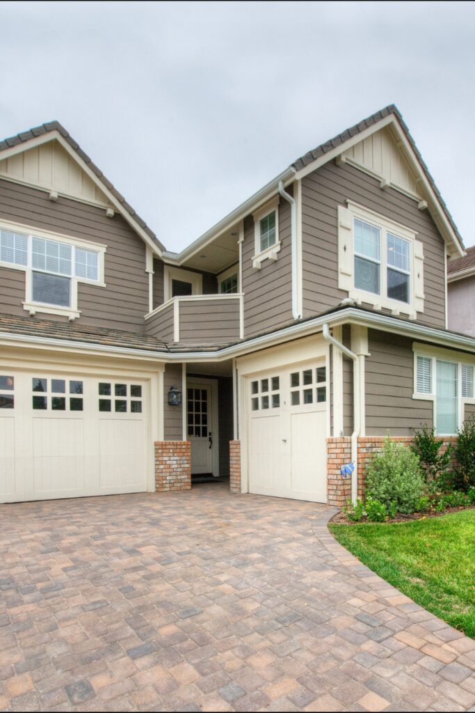 Two-story exterior with gray siding, carriage-style garage doors, brick accents and paver driveway