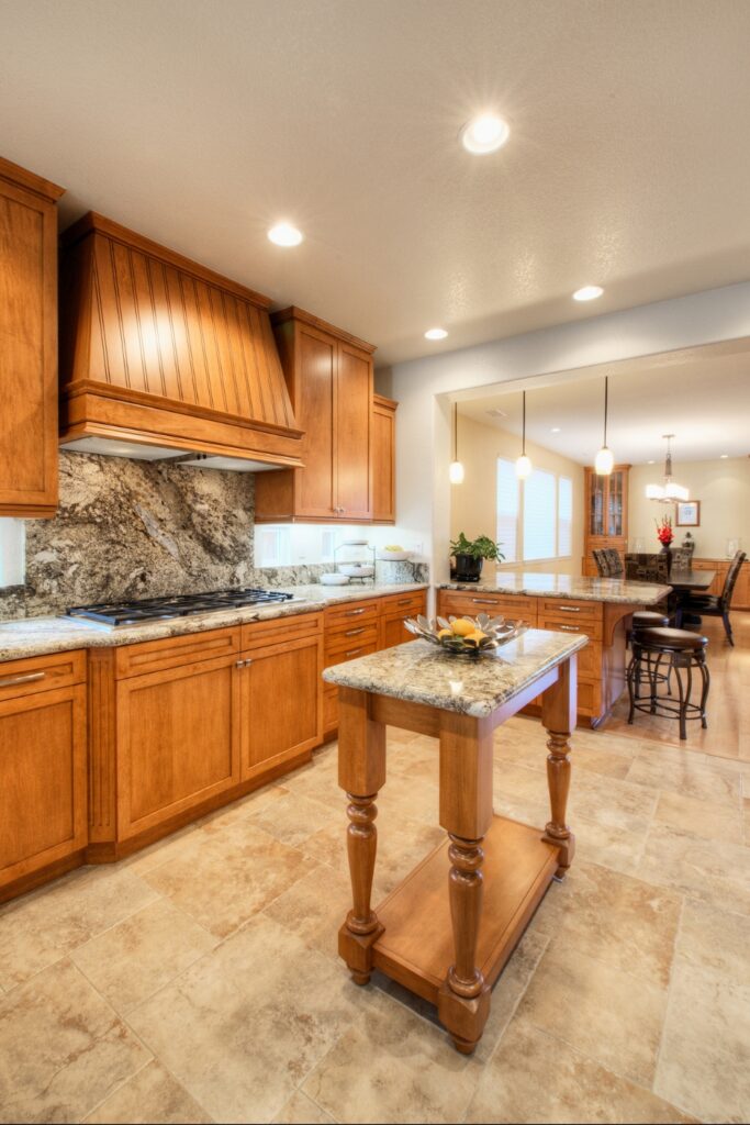 Kitchen with wood range hood, granite backsplash and travertine tile floor opening to the dining area