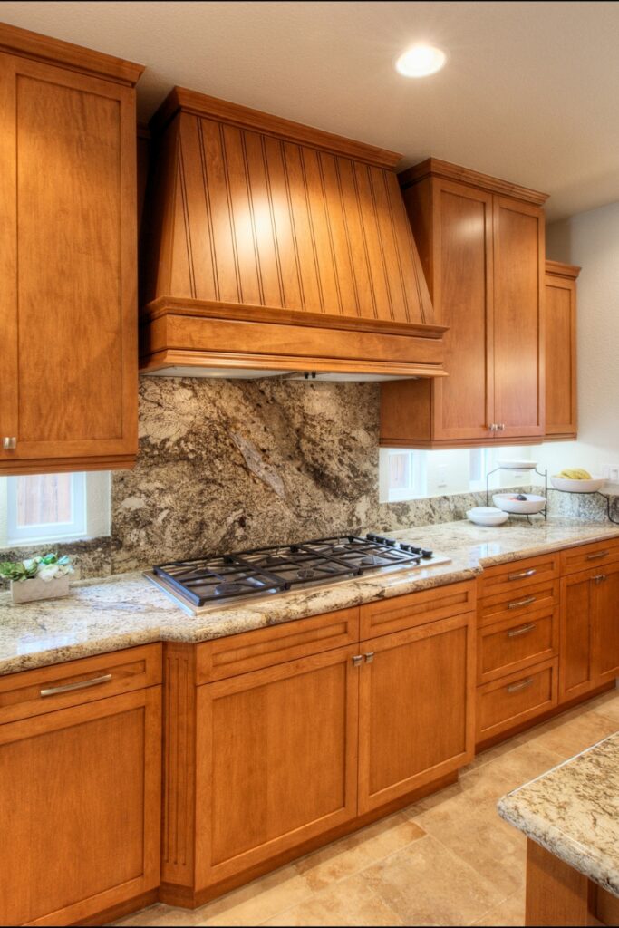 Gas cooktop with granite slab backsplash framed by wood cabinetry and range hood