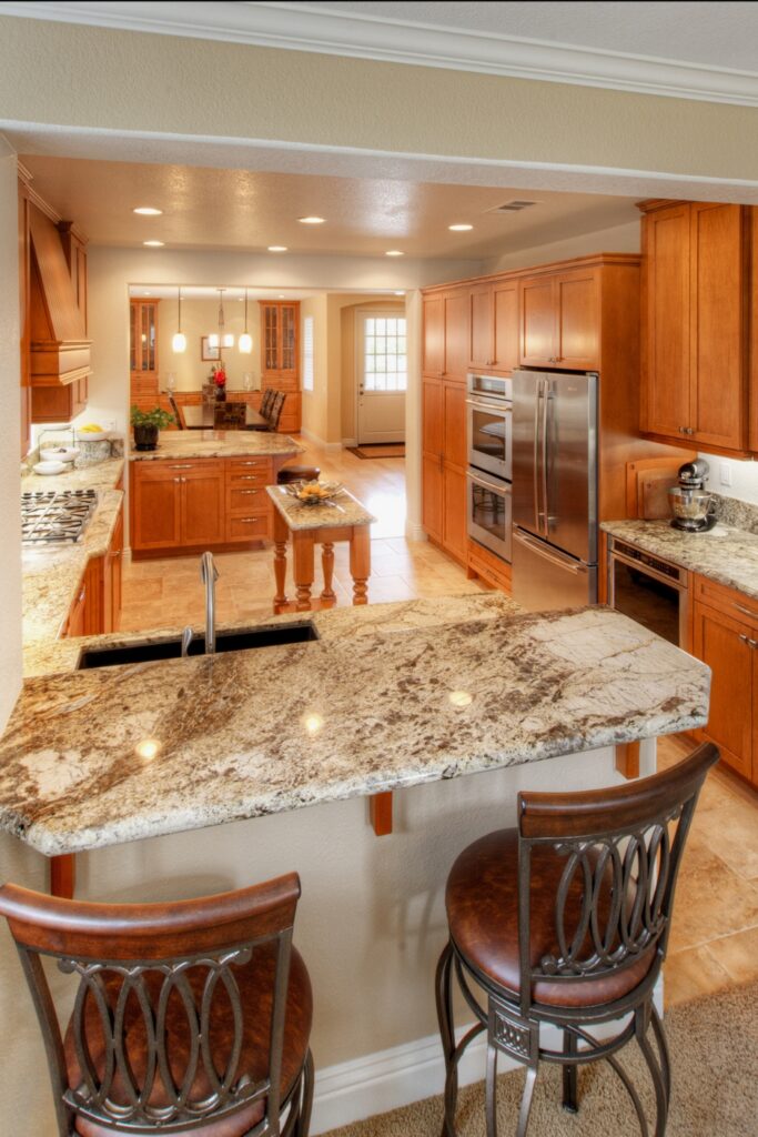 Kitchen peninsula with granite counter and sink, stainless double ovens and refrigerator beyond
