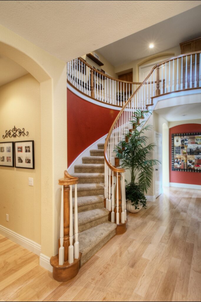 Curved staircase with wood and white balusters, carpeted treads and hardwood foyer flooring