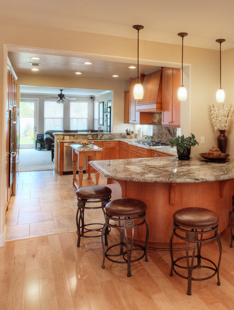 Remodeled Carmel Valley kitchen with granite peninsula, wood cabinetry and pendant lighting open to the living room
