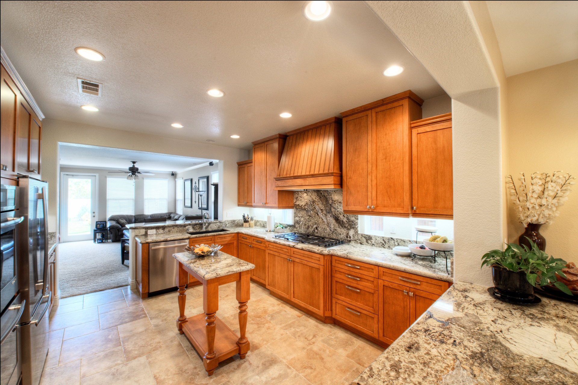 Remodeled kitchen with granite backsplash, wood cabinetry, stainless appliances and travertine floors