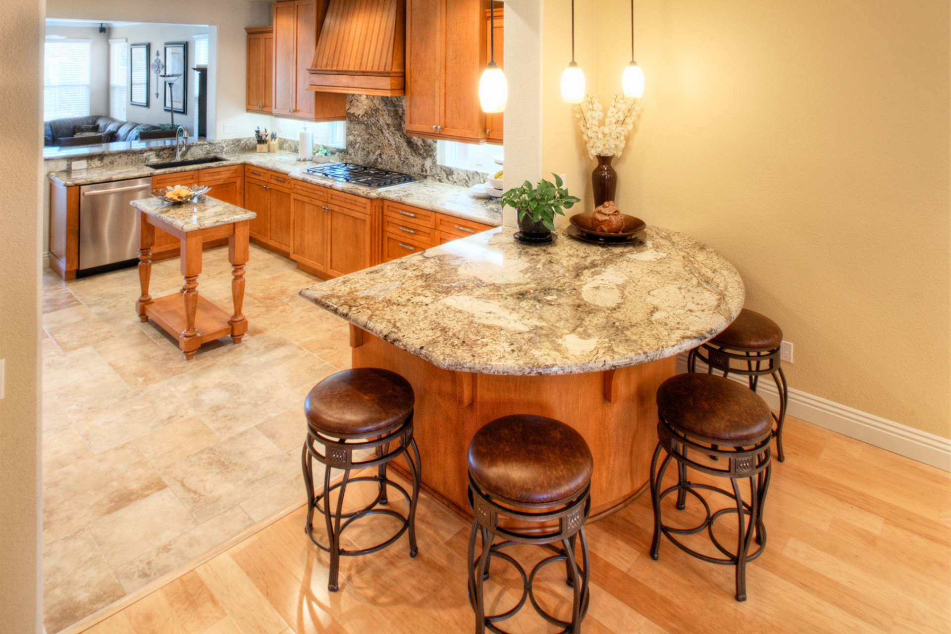 Curved granite kitchen peninsula with bar stools, pendant lighting and view to the cooktop and range hood
