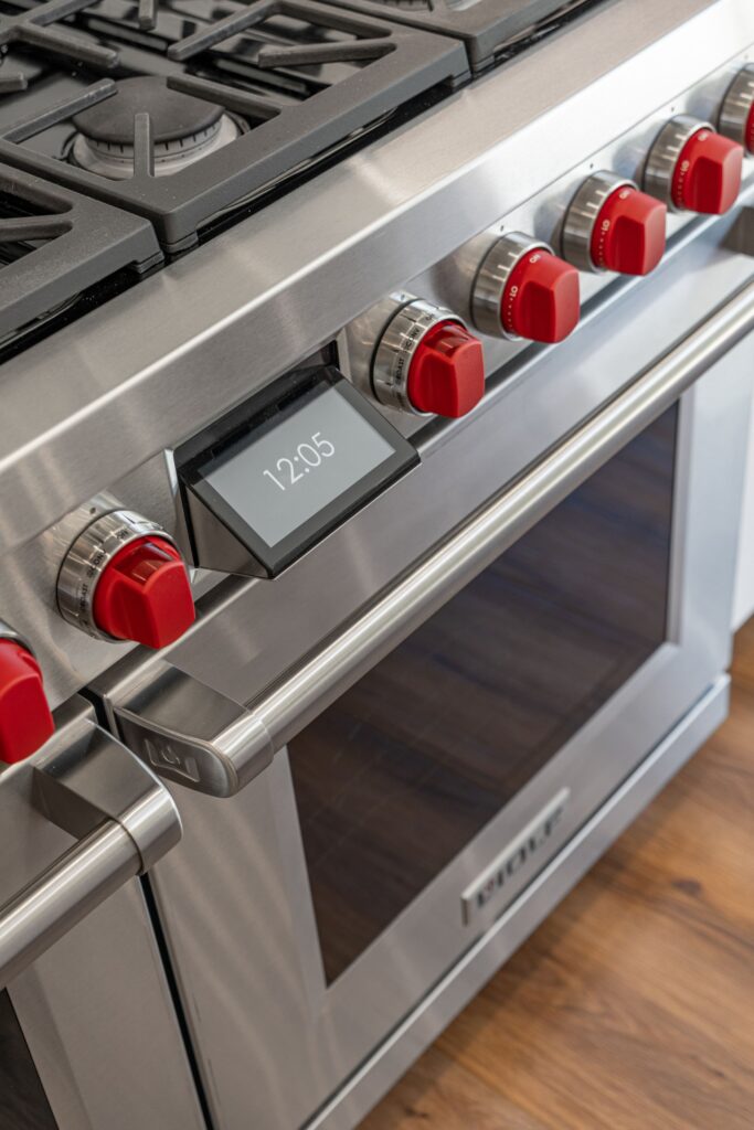 Stainless steel kitchen range with red control knobs, gas burners and digital display