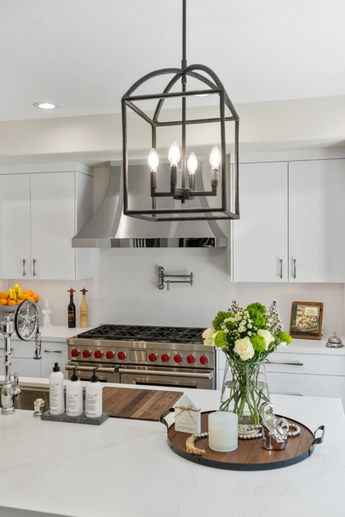 Kitchen island beneath black lantern pendant with white cabinetry, stainless range and sculpted vent hood