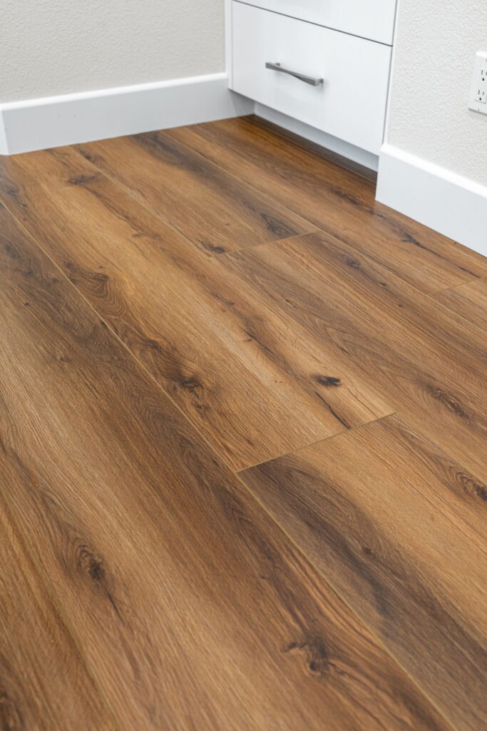 [Warm wood-look plank flooring beside white kitchen cabinetry and wide base trim