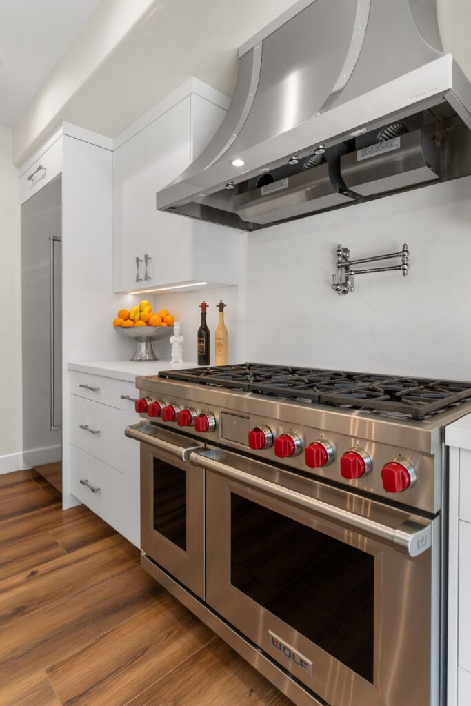 Stainless range with red knobs, pot filler, custom vent hood and white cabinetry in remodeled kitchen