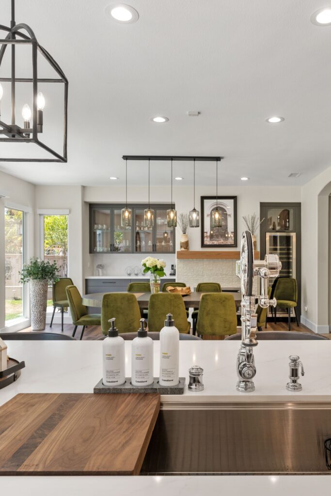 Kitchen island sink with polished chrome faucet overlooking dining room cabinetry, pendant lights and fireplace