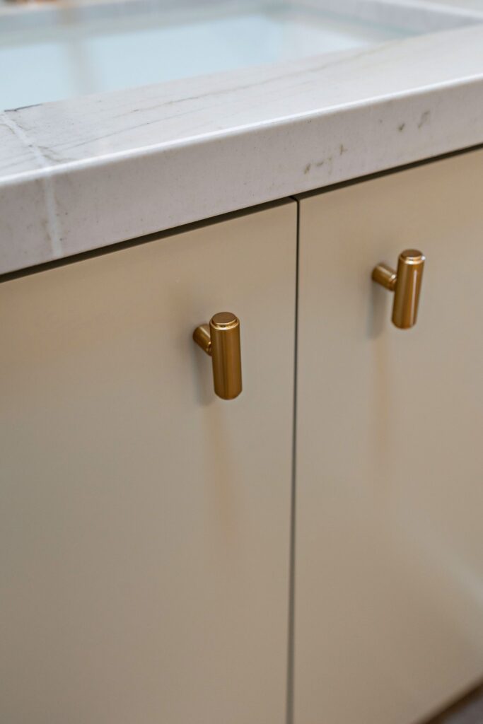 Close-up of flat-panel bathroom cabinetry with brass knobs and a light veined stone countertop.