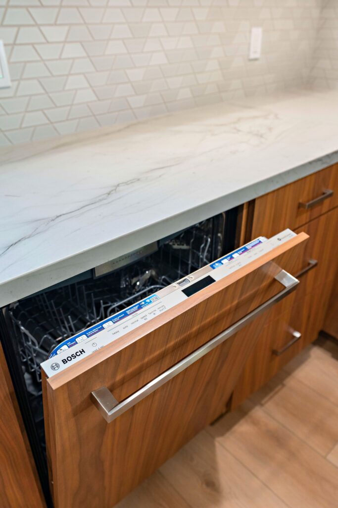 Panel-front dishwasher integrated into walnut kitchen cabinetry beneath a light veined countertop.