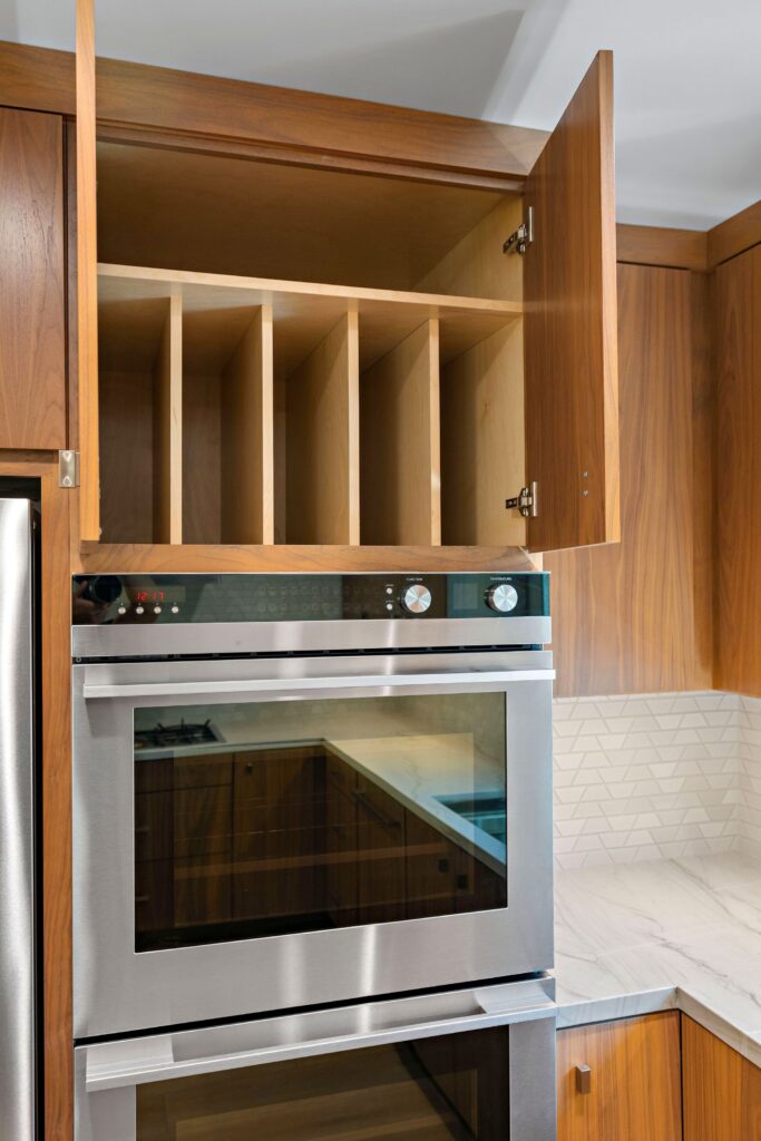 Built-in stainless wall ovens with walnut cabinetry and vertical storage dividers above.