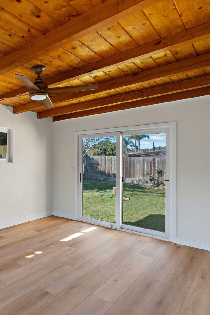 Living space with exposed wood ceiling beams, ceiling fan, sliding glass doors and wide-plank flooring.