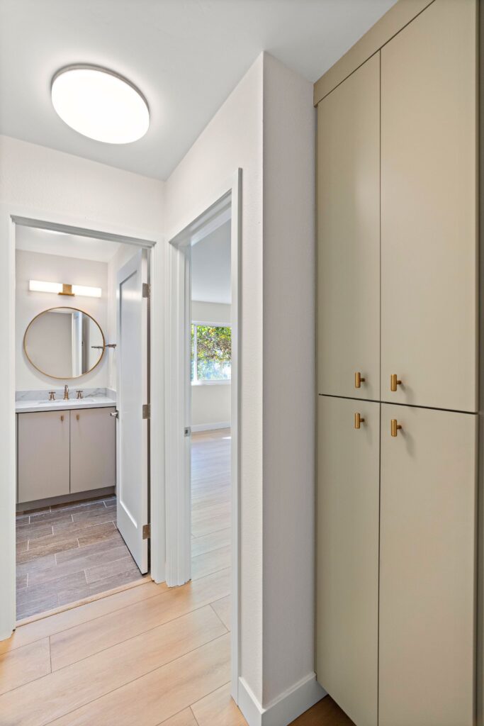 Hallway with tall built-in storage cabinets, brass hardware, light wood flooring and adjacent bathroom.