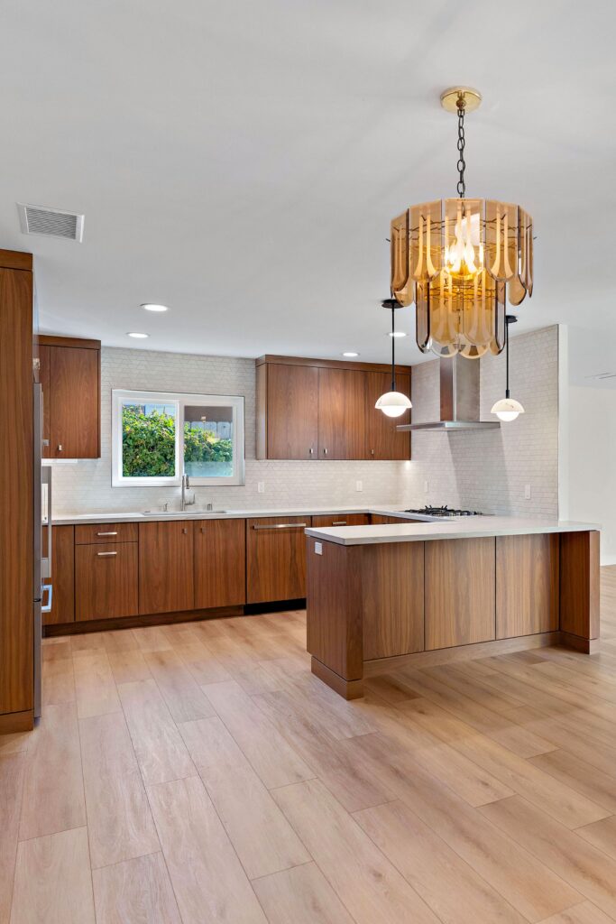 Clairemont kitchen with walnut cabinetry, peninsula seating, white counters, geometric backsplash and statement lighting.