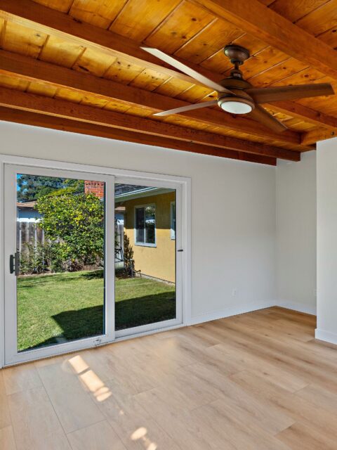 Clairemont living space with exposed wood ceiling beams, ceiling fan, sliding glass doors and light wood flooring. Banner image alt tag: