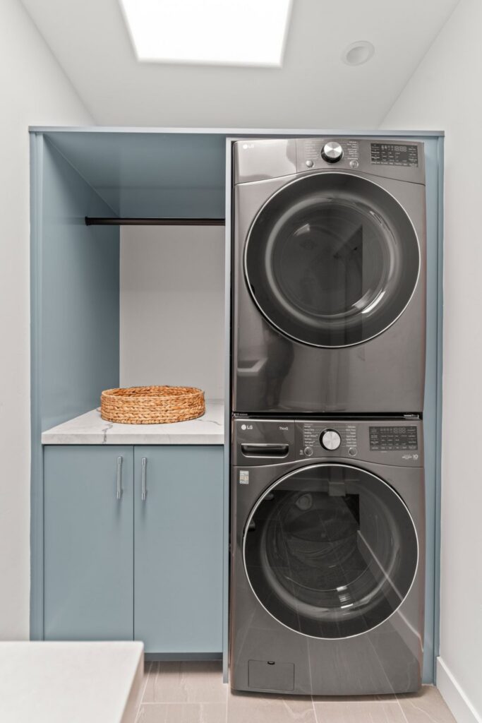Converted laundry room with stacked washer and dryer, blue cabinetry, countertop and skylight