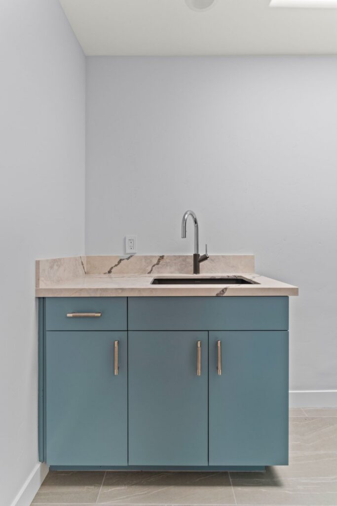 Laundry room sink with blue base cabinetry, stone countertop, black faucet and brass hardware