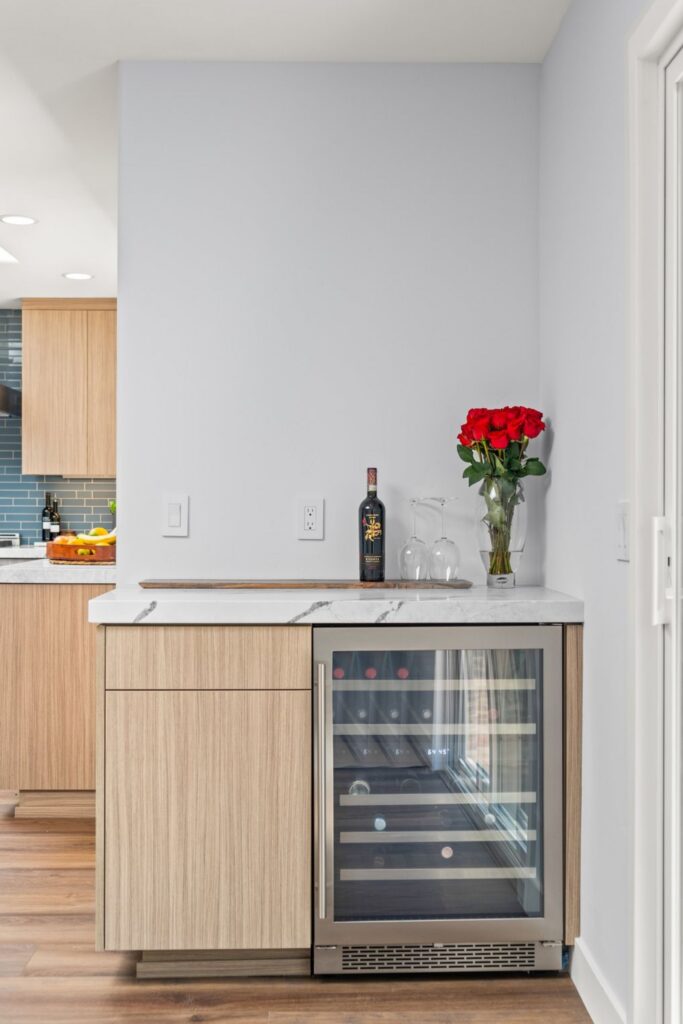 Built-in beverage refrigerator with light wood cabinetry and white veined stone countertop
