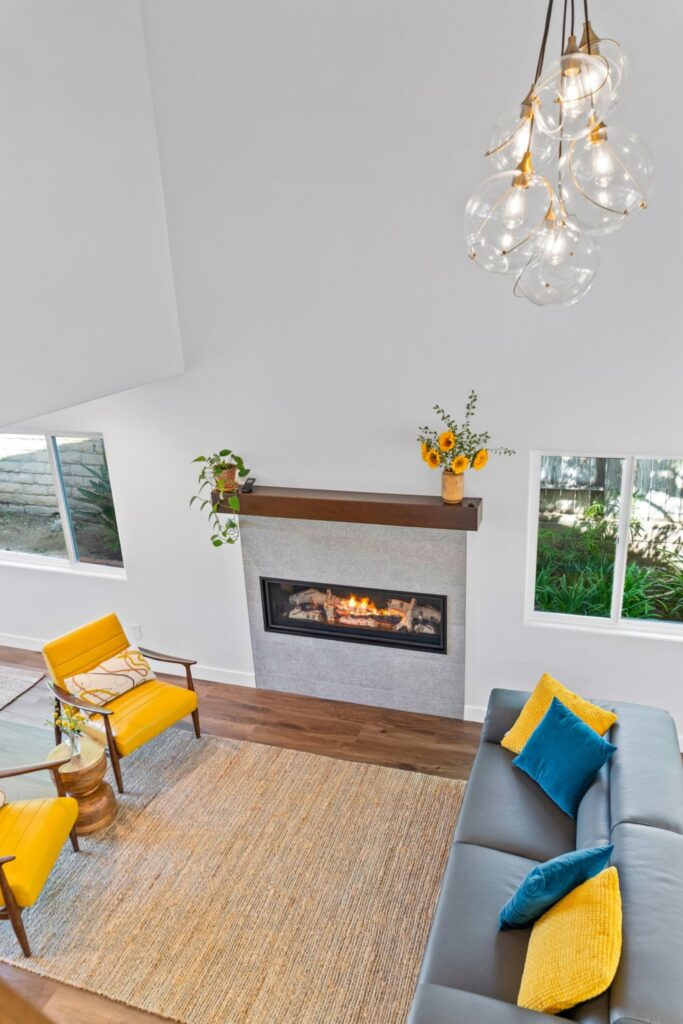 Two-story family room with linear fireplace, wood mantel, gray sofa and glass globe chandelier