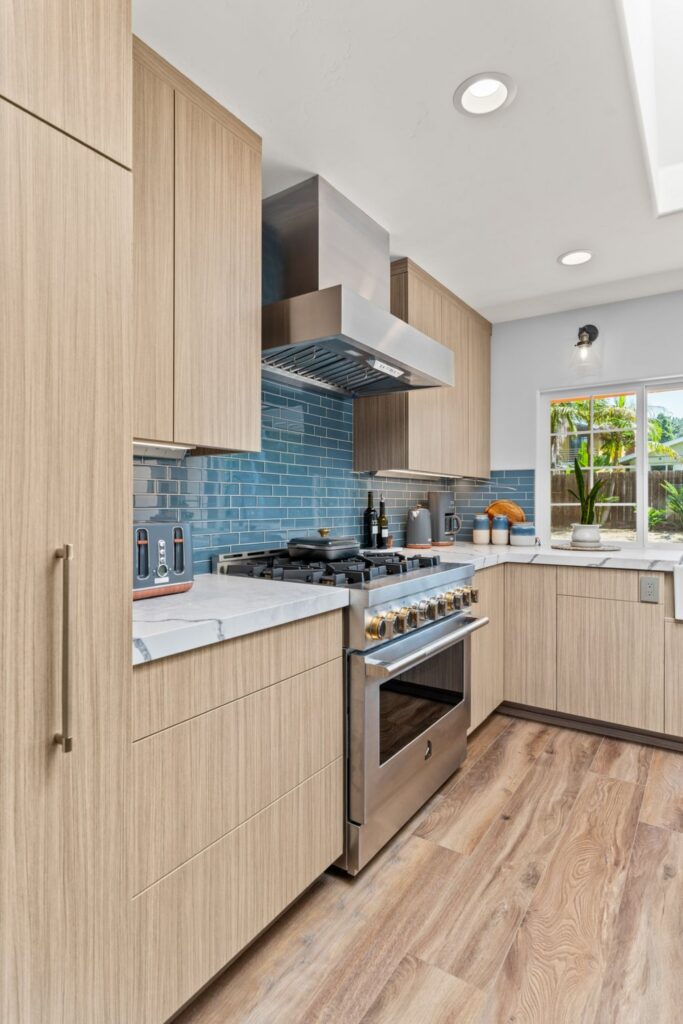 Del Mar kitchen with light wood cabinetry, stainless range, blue tile backsplash and stone countertops