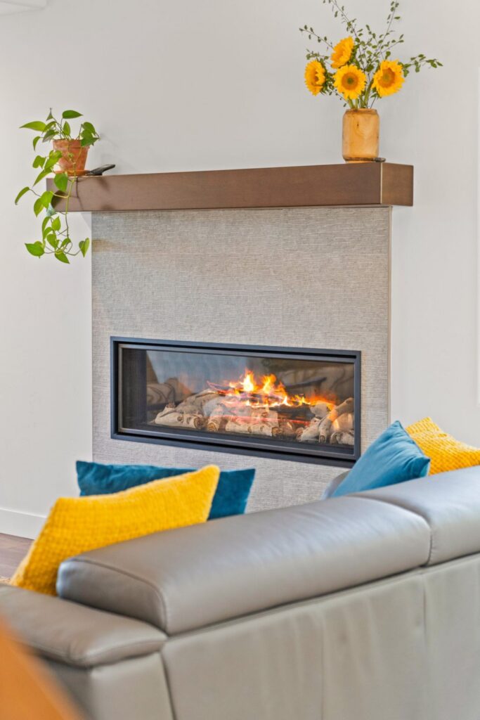 Linear fireplace with textured gray surround, dark wood mantel and gray sofa with colorful pillows