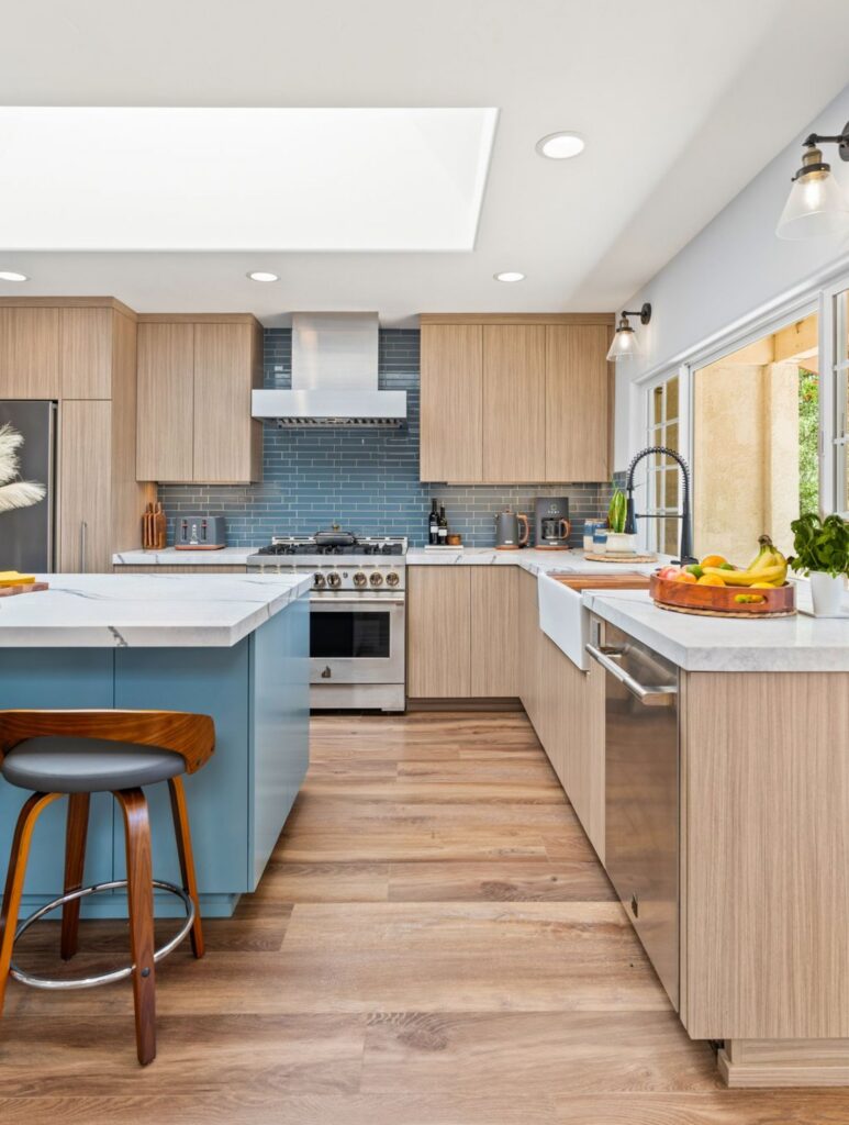Del Mar open kitchen with blue island, light wood cabinetry, blue tile backsplash, farmhouse sink and skylight.